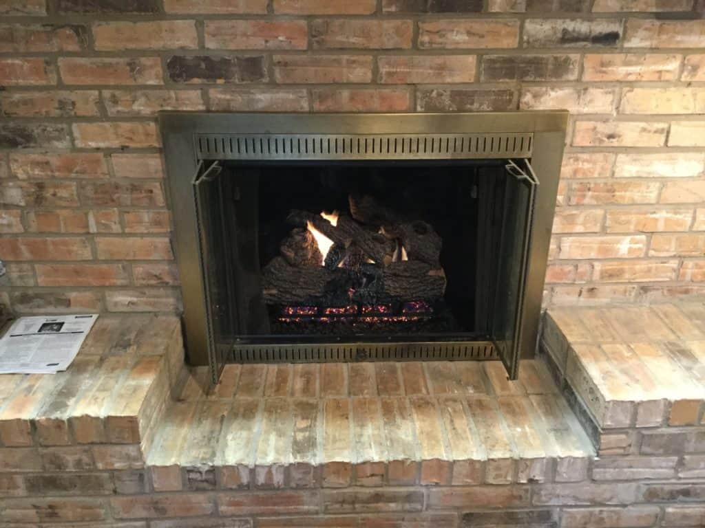 Fireplace burning with newly installed charred gas logs and custom glass fireplace doors by Masters Services 