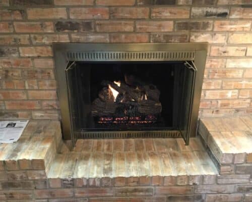 Fireplace burning with newly installed charred gas logs and custom glass fireplace doors by Masters Services